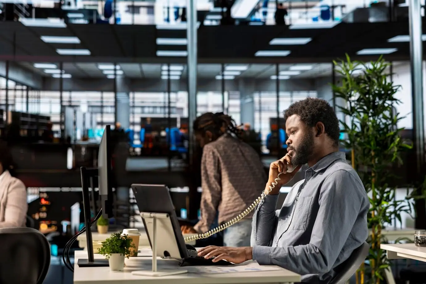 Afroamerikanischer Investor führt an seinem Schreibtisch ein Festnetztelefonat und verhandelt über Gelder.